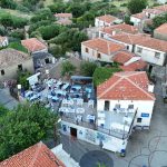 Explore a serene village in Gökçeada, Türkiye with charming red-tiled roofs and outdoor dining spaces.